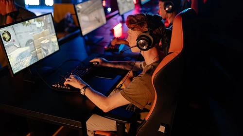 Een esports-speler die meerdere beeldschermen en een headset gebruikt in een competitieve gamingomgeving met neonverlichting.
