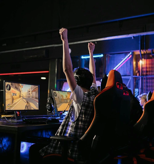 Een gamer die zijn handen in de lucht steekt om zijn overwinning te vieren, zittend achter een gamingopstelling met meerdere beeldschermen.