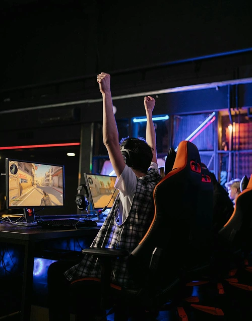Een gamer die zijn handen in de lucht steekt om zijn overwinning te vieren, zittend achter een gamingopstelling met meerdere beeldschermen.
