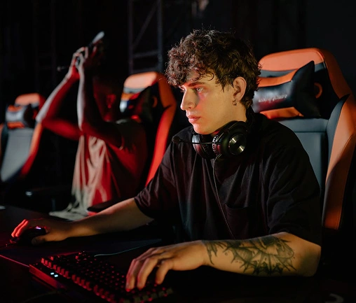 Een geconcentreerde mannelijke gamer met een headset op, die op een pc speelt in een donkere gamekamer met neonverlichting.